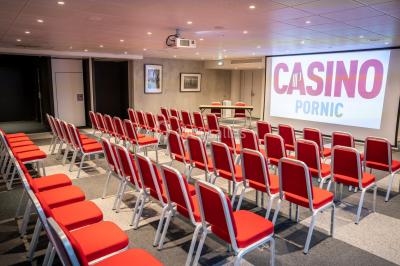 Bâtiment moderne en bord de rivière, entouré de verdure, avec un pont piétonnier au premier plan.