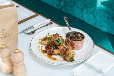 Bâtiment moderne en bord de rivière, entouré de verdure, avec un pont piétonnier au premier plan.