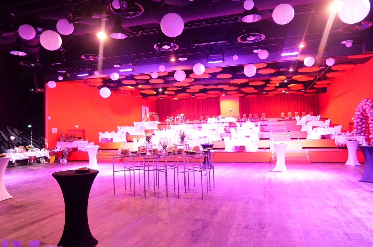 Salle de réception décorée avec des tables dressées, éclairage rose et plafond orné de suspensions rondes blanches.