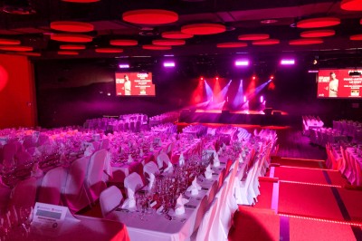 Bâtiment moderne en bord de rivière, entouré de verdure, avec un pont piétonnier au premier plan.