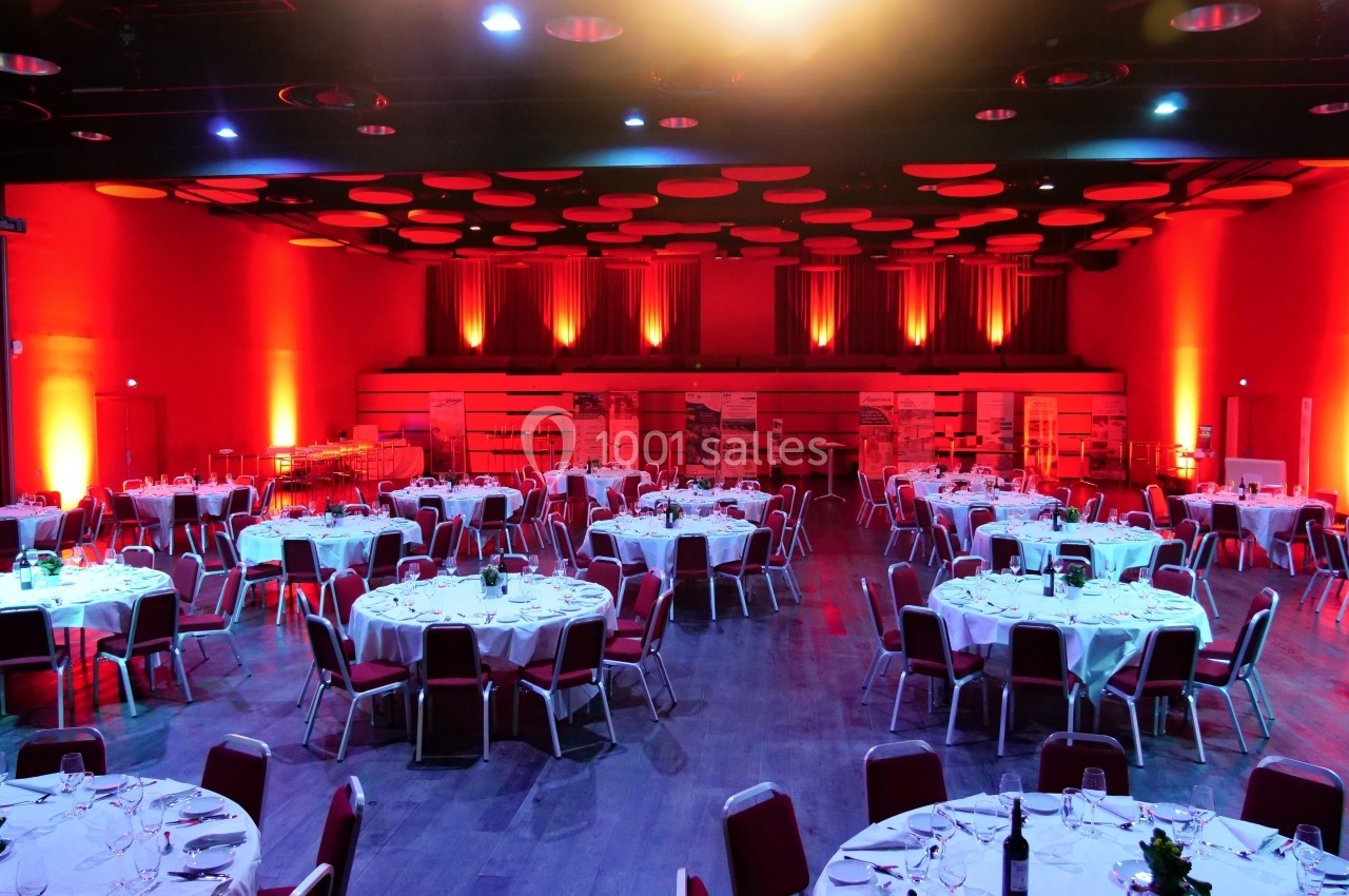 Salle de réception éclairée en rouge avec des tables rondes dressées pour un événement.