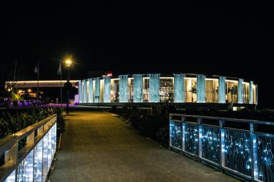 Bâtiment circulaire moderne illuminé la nuit, avec un chemin éclairé et des rampes décorées de lumières.
