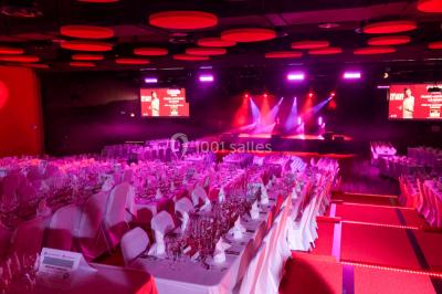 Bâtiment circulaire moderne illuminé la nuit, avec un chemin éclairé et des rampes décorées de lumières.