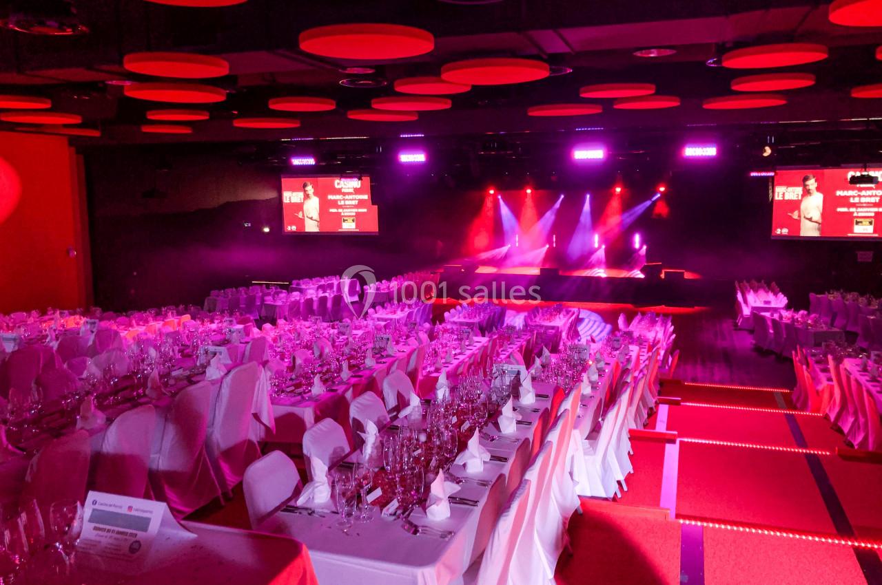 Salle de réception avec tables dressées, éclairage rouge et scène équipée de projecteurs lumineux.