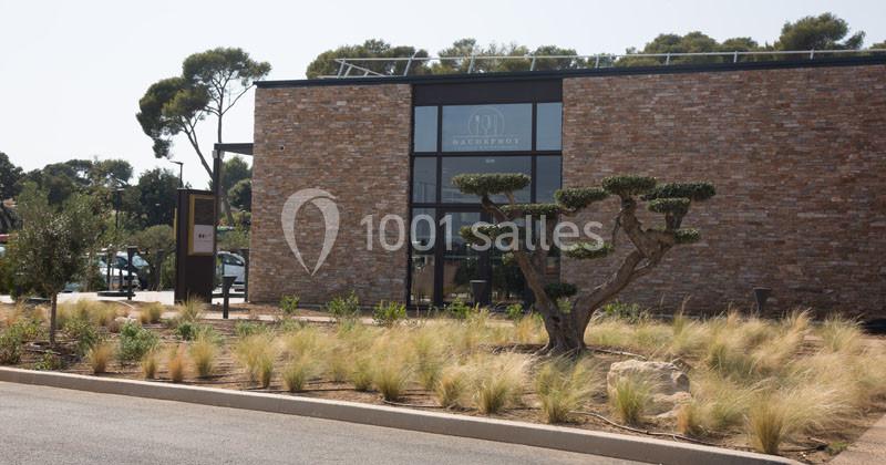 Façade d'un bâtiment moderne en pierre avec un jardin paysager composé d'herbes hautes et d'arbres taillés.