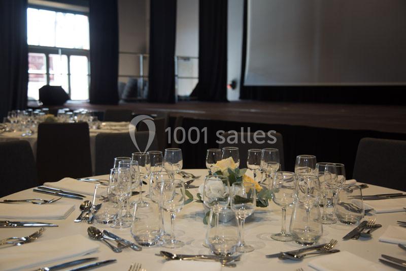 Table dressée avec nappes blanches, verres et couverts, devant une scène dans une salle de réception.