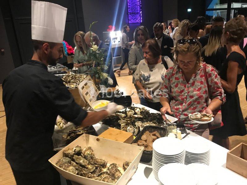 Un chef sert des huîtres fraîches à des convives lors d'un buffet dans un cadre intérieur animé.