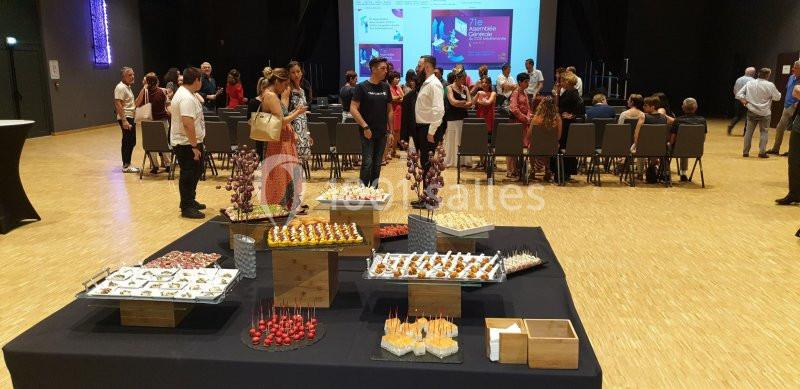 Buffet de réception avec amuse-bouches variés au premier plan, et participants debout ou assis en arrière-plan.