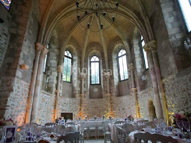 Salle voûtée en pierre avec grandes fenêtres, tables dressées pour un événement, éclairage chaleureux.