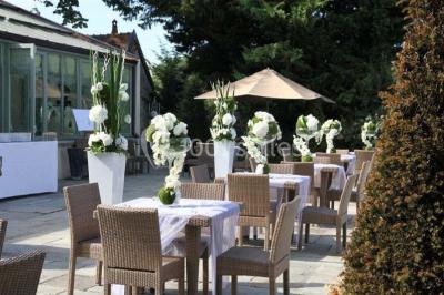 Un couple en tenue de mariage marche dans une allée extérieure décorée, entourée de chaises et de pétales de fleurs.