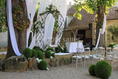 Un couple en tenue de mariage marche dans une allée extérieure décorée, entourée de chaises et de pétales de fleurs.