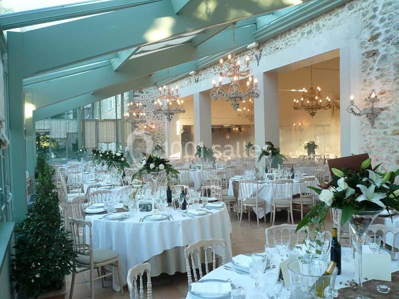 Salle de réception élégante avec tables rondes dressées, décor floral et grandes baies vitrées laissant entrer la lumière.