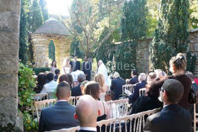 Un couple en tenue de mariage marche dans une allée extérieure décorée, entourée de chaises et de pétales de fleurs.