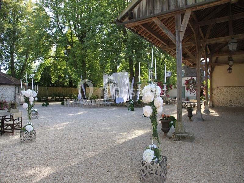 Cour extérieure aménagée pour un événement, avec décorations florales, chaises alignées et structure en bois ouverte.