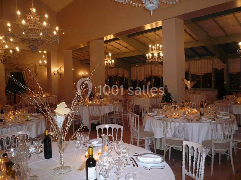 Salle de réception élégamment décorée avec des tables rondes dressées, chandeliers et éclairage chaleureux.