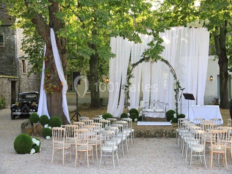 Cérémonie en plein air avec arche décorée de voilages blancs, chaises alignées et voiture ancienne en arrière-plan.