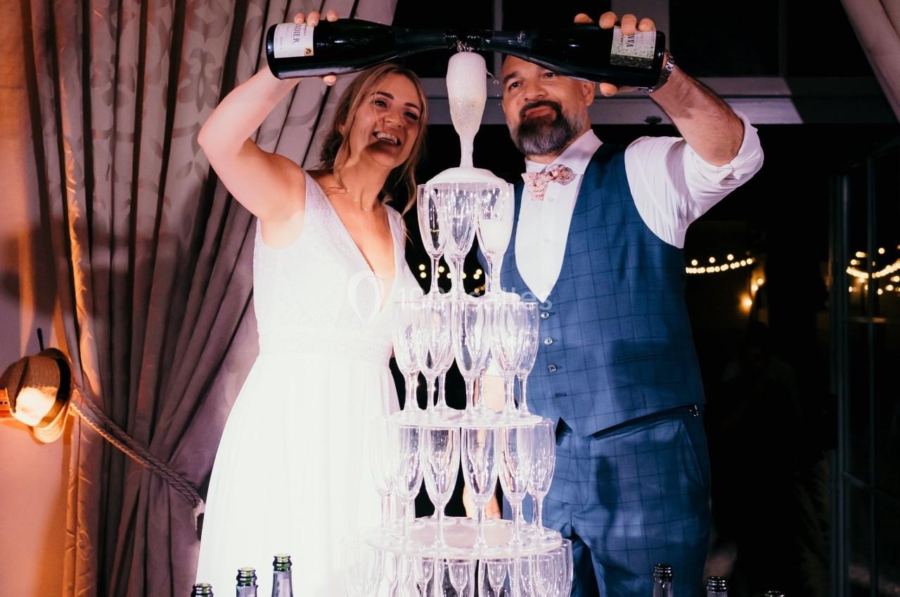 Un couple verse du champagne dans une pyramide de flûtes lors d'une célébration festive en intérieur.