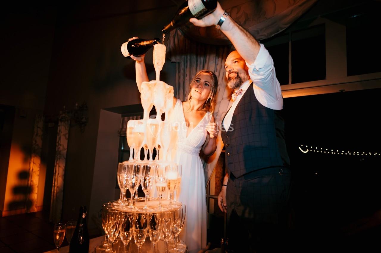 Un couple verse du champagne dans une pyramide de verres lors d'une célébration festive.