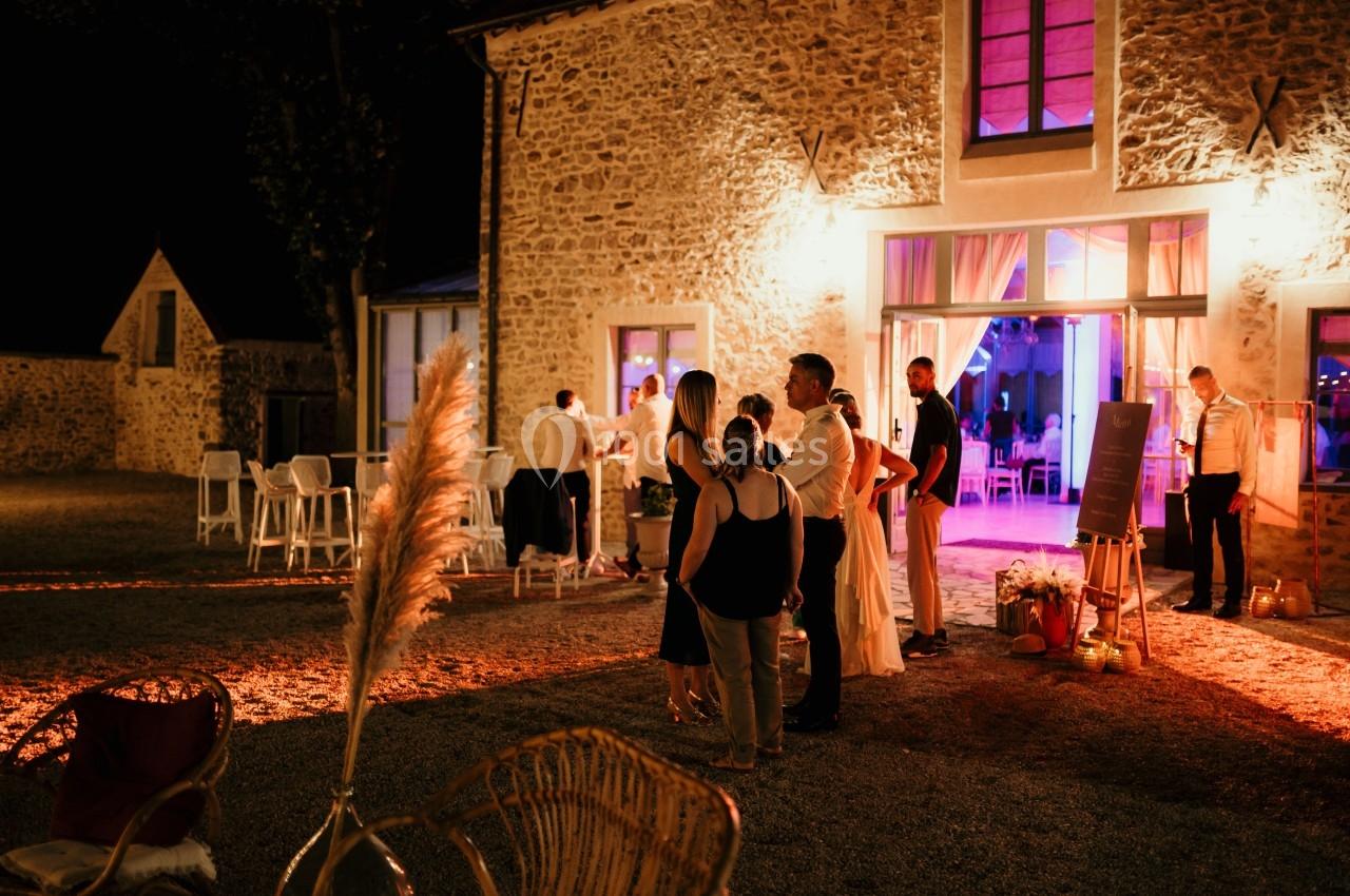 Groupe de personnes discutant devant un bâtiment en pierre éclairé, avec une ambiance festive en soirée.