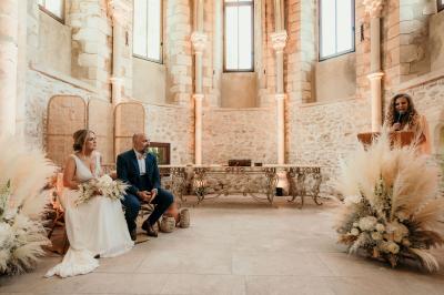 Un couple en tenue de mariage marche dans une allée extérieure décorée, entourée de chaises et de pétales de fleurs.