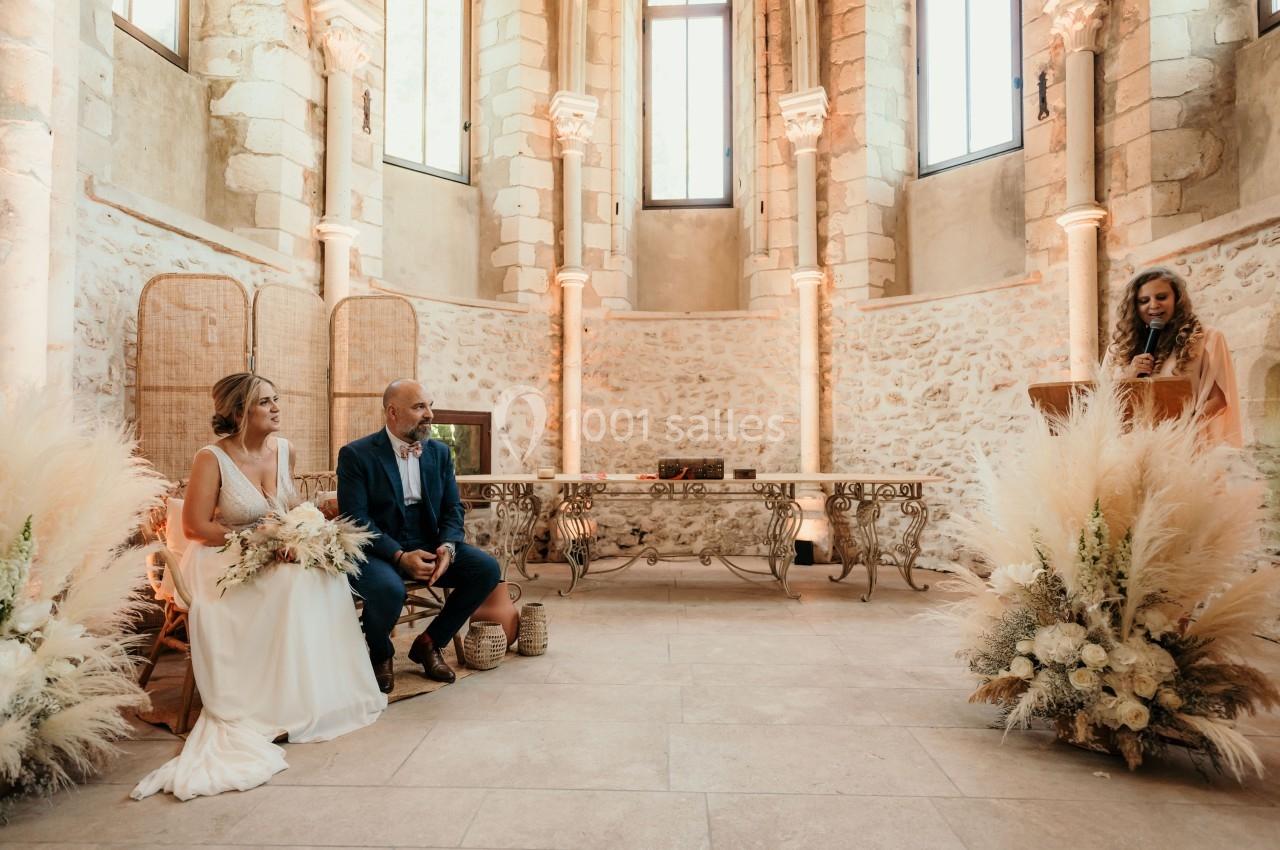 Un couple assis dans une salle lumineuse au style ancien, écoutant une femme debout à un pupitre.