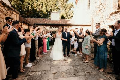 Un couple en tenue de mariage marche dans une allée extérieure décorée, entourée de chaises et de pétales de fleurs.
