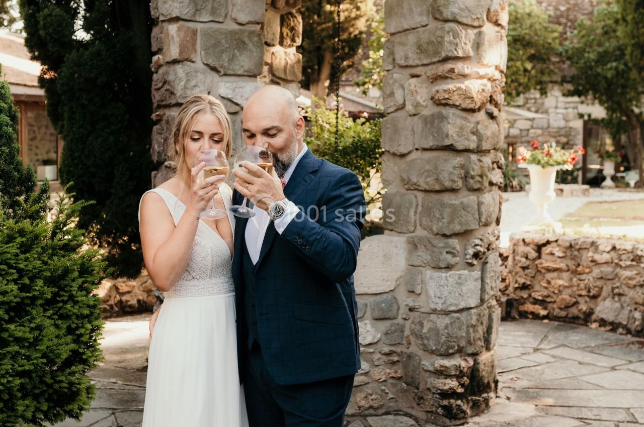 Un couple en tenue de mariage boit un verre devant un puits en pierre dans un jardin.