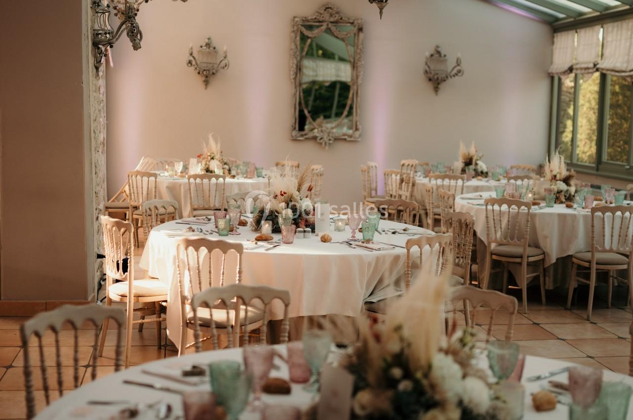 Salle de réception lumineuse avec tables décorées de fleurs, vaisselle colorée et chandeliers suspendus.