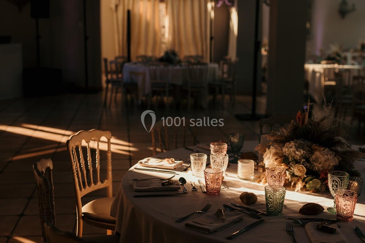 Salle de réception éclairée par une lumière tamisée, table dressée avec vaisselle et décoration florale.