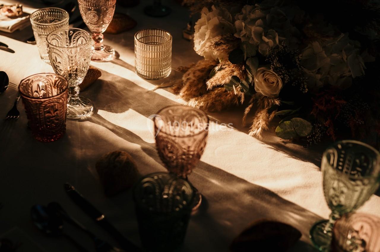 Table décorée avec des verres colorés, des couverts et un centre de table floral, éclairée par une lumière douce.