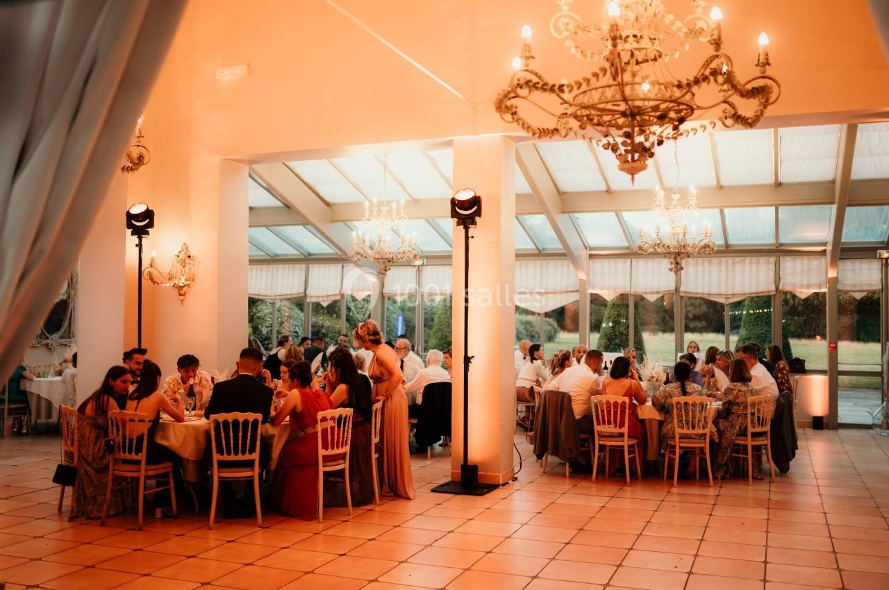 Des convives assis à des tables rondes dans une salle lumineuse décorée de lustres et baignée d'une lumière chaleureuse.