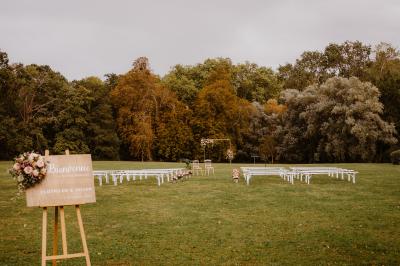 Un couple en tenue de mariage marche dans une allée extérieure décorée, entourée de chaises et de pétales de fleurs.