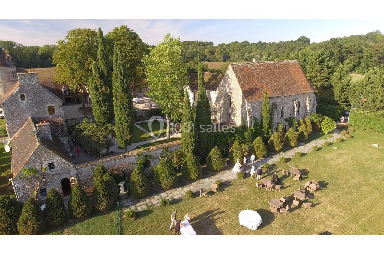 Vue aérienne d'un domaine avec une chapelle en pierre, des jardins aménagés et des tables installées sur la pelouse.