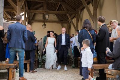 Un couple en tenue de mariage marche dans une allée extérieure décorée, entourée de chaises et de pétales de fleurs.