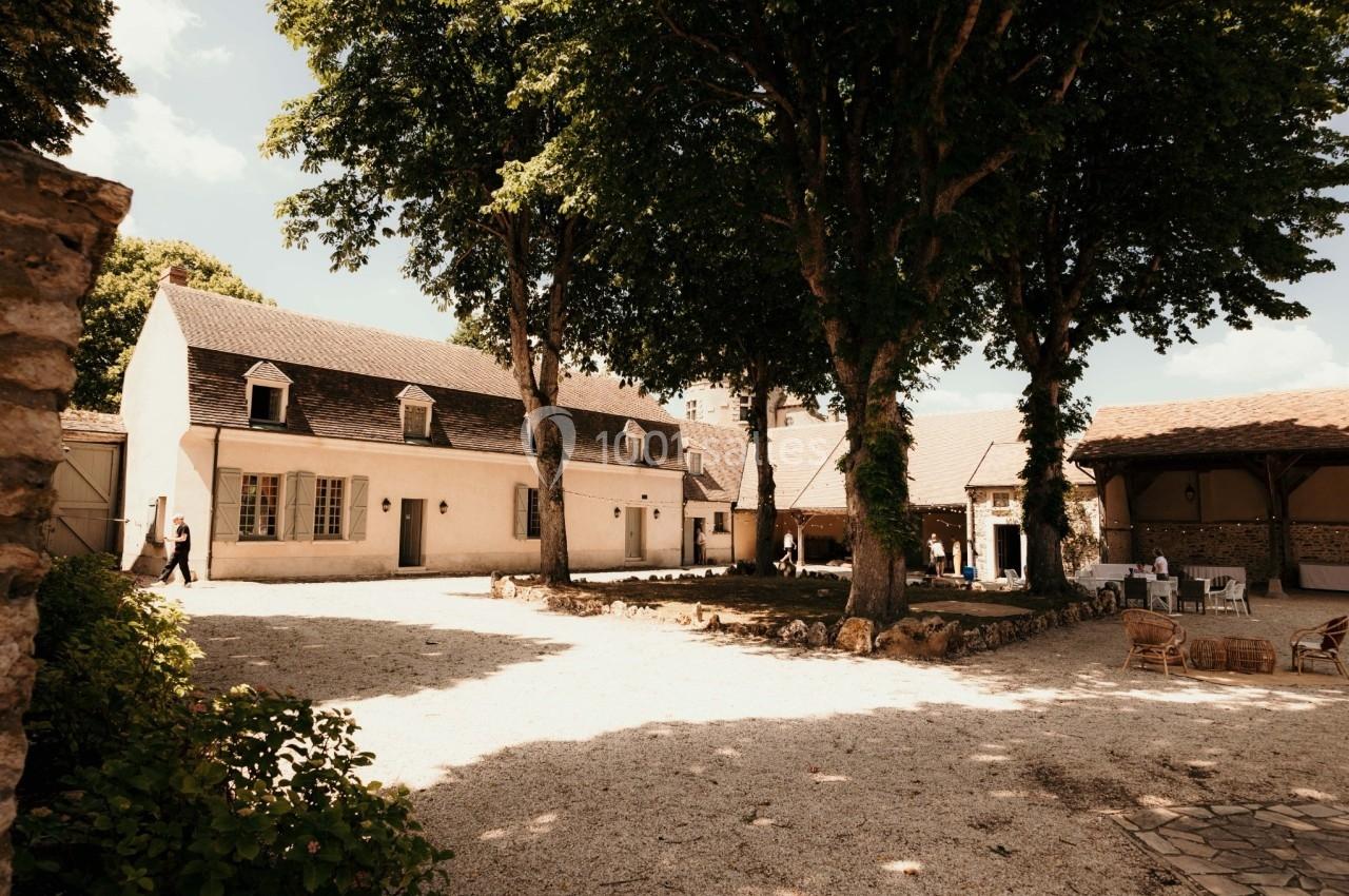 Cour intérieure avec une maison en pierre, des arbres ombrageant l'espace et quelques meubles d'extérieur.