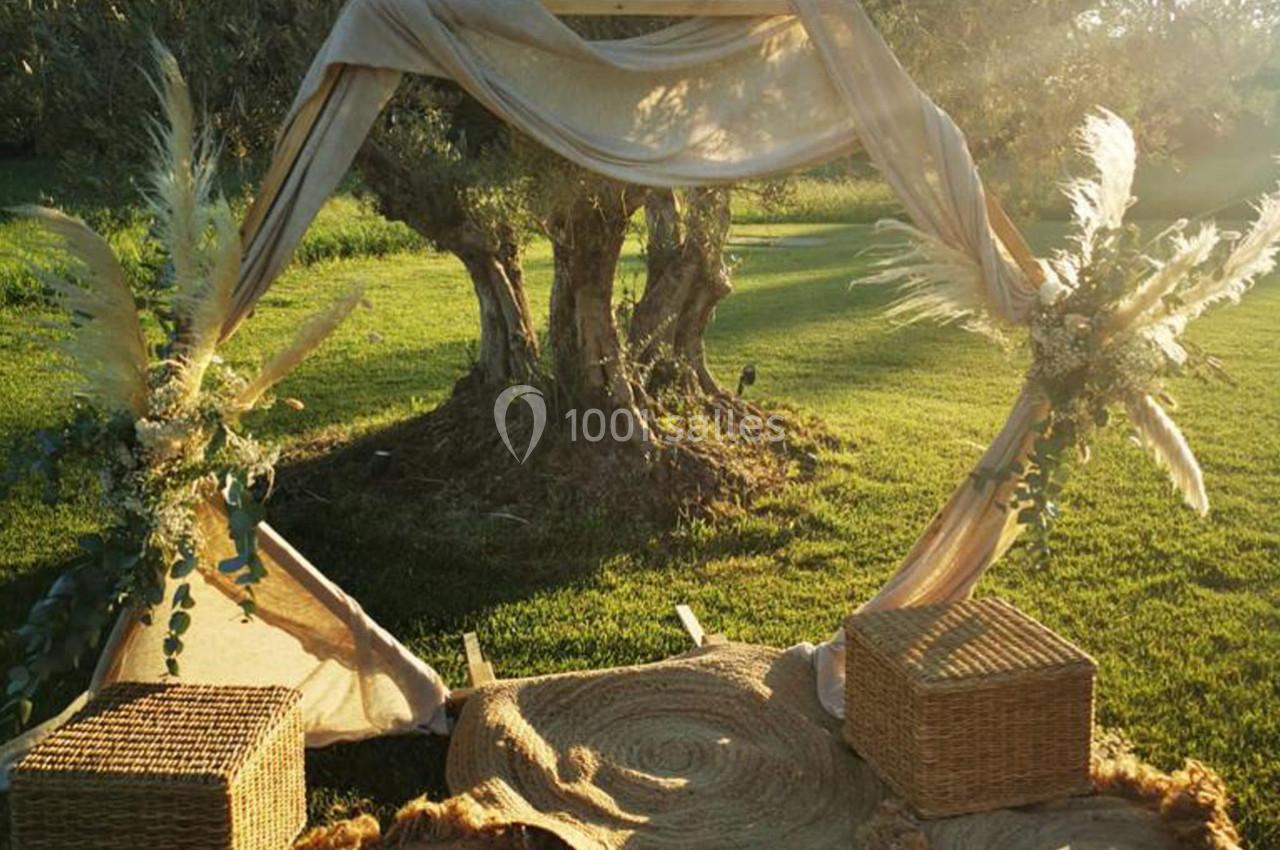 Arche décorative en tissu beige avec ornements végétaux, installée sur une pelouse au coucher du soleil.