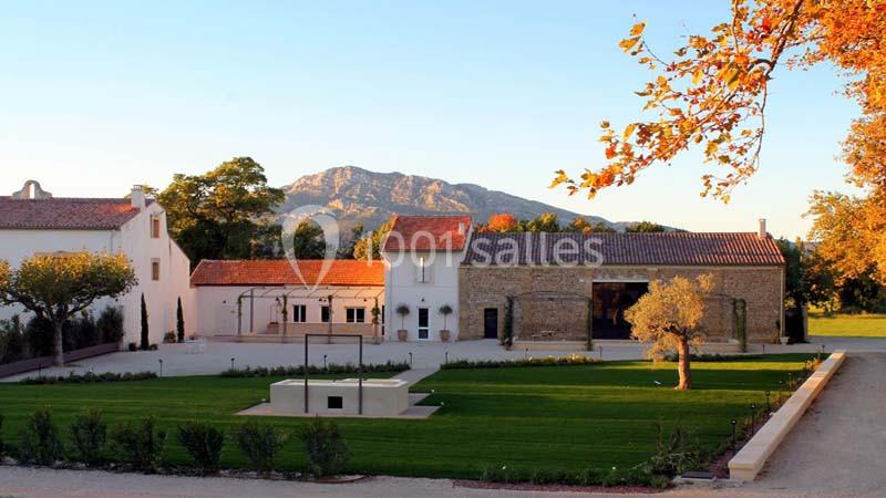 Cour d'une propriété avec bâtiments en pierre, pelouse aménagée, arbres et montagnes en arrière-plan.