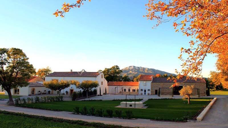 Bâtiments en pierre entourés de pelouses et d'arbres aux feuilles d'automne, avec une colline en arrière-plan.