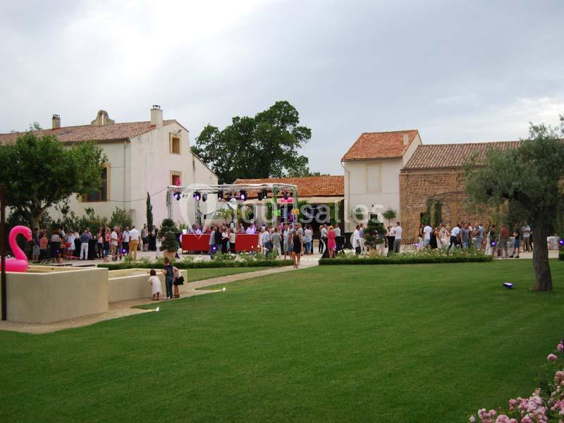 Groupe de personnes rassemblées dans une cour verdoyante avec des bâtiments en pierre et des décorations festives.