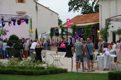 Vue aérienne d'une fête nocturne en extérieur avec éclairages violets, scène musicale et invités rassemblés.