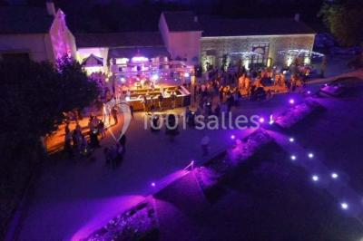 Vue aérienne d'une fête nocturne en extérieur avec éclairages violets, scène musicale et invités rassemblés.