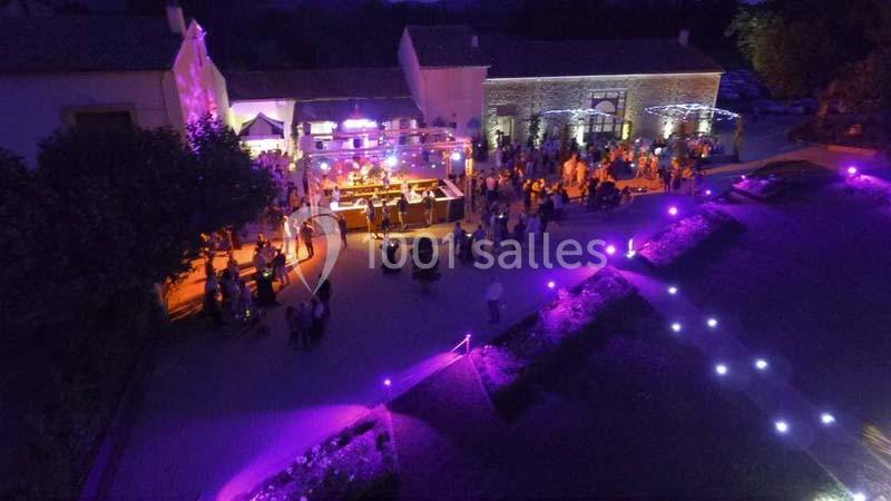 Vue aérienne d'une fête nocturne en extérieur avec éclairages violets, scène musicale et invités rassemblés.