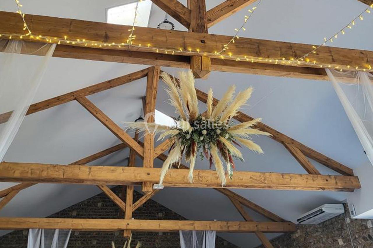 Structure en bois apparente d'un plafond de salle, décorée de guirlandes lumineuses et d'une suspension florale.