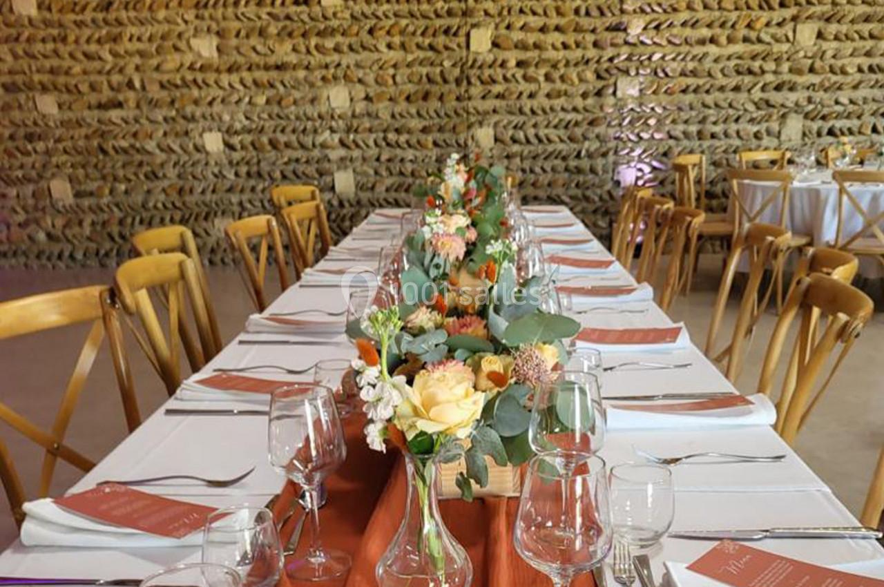 Table dressée avec nappes blanches, chemins de table orange, bouquets de fleurs et vaisselle élégante dans une salle en…