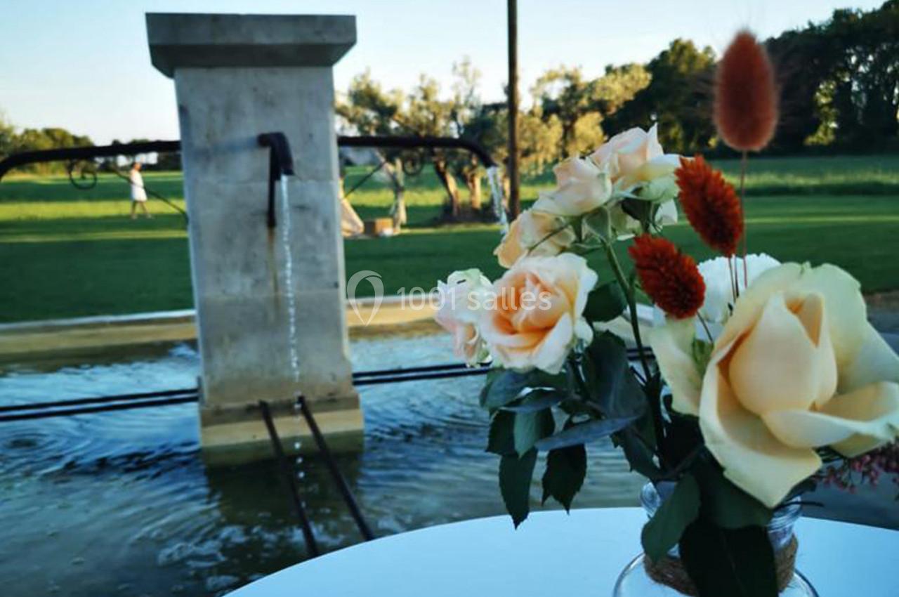Vase avec des roses jaunes et fleurs rouges sur une table, devant une fontaine et un paysage verdoyant.