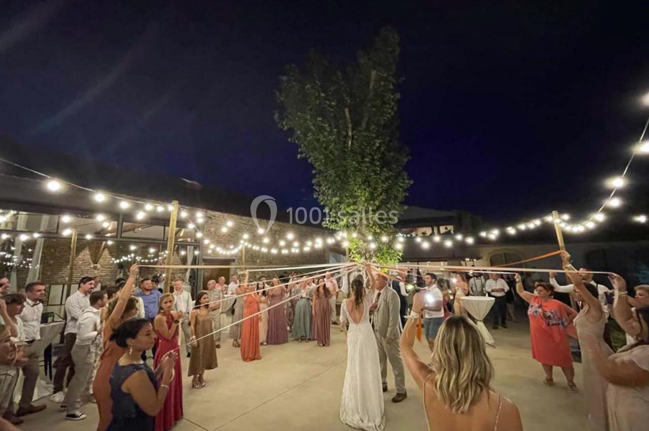Des invités dansent autour d'un couple sous des guirlandes lumineuses, tenant des rubans reliés à un arbre.