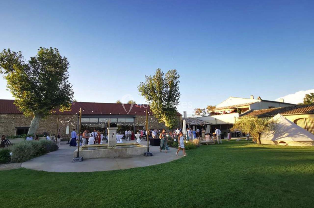 Groupe de personnes rassemblées près d'une fontaine dans une cour verdoyante, entourée de bâtiments en pierre.