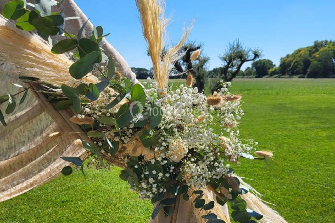 Arrangement floral avec eucalyptus, gypsophile et herbes de la pampa fixé sur un tissu beige, en extérieur verdoyant.