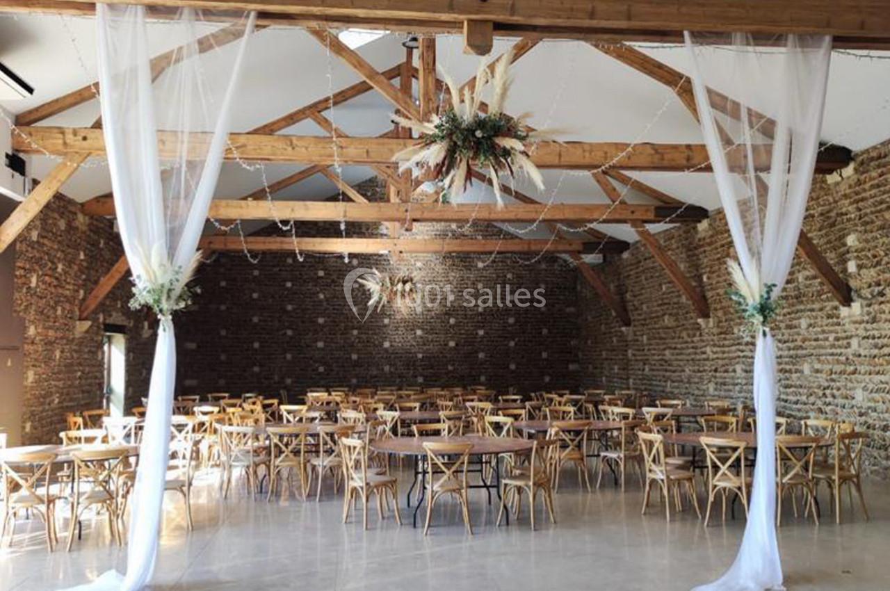Salle de réception avec murs en briques, poutres apparentes, tables en bois et décorations florales suspendues.