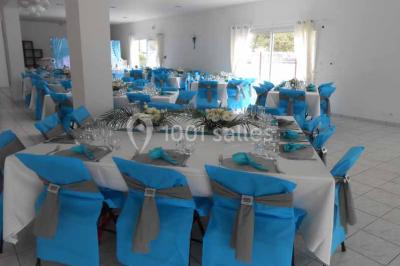 Salle de réception décorée avec des tables dressées, nappes blanches, chaises ornées de nœuds violets et centres de table…